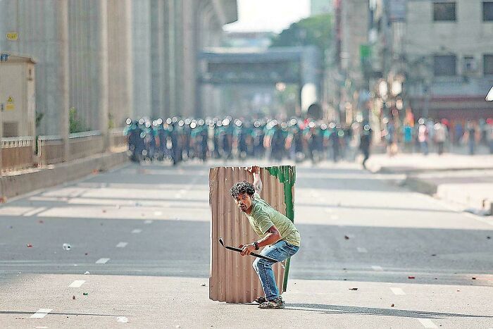 Man holding shield crouching in street, resembling a Renaissance masterpiece captured in a candid moment.