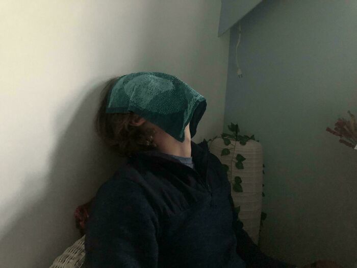 Person leaning back with a towel covering their face in a dimly lit room, an accidental Renaissance style photo.