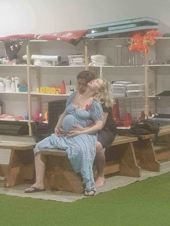 Pregnant woman leaning back on a bench with another person supporting her, captured in an accidental renaissance photo moment.