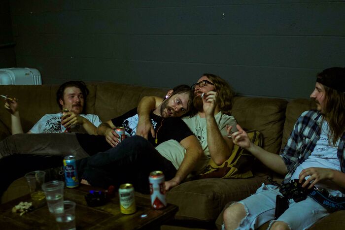 Four friends casually relaxing on a couch with drinks, capturing a moment resembling a Renaissance masterpiece scene