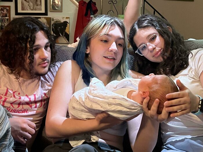 Three young adults sitting on a couch holding a baby, capturing a tender accidental Renaissance moment in a cozy home setting.