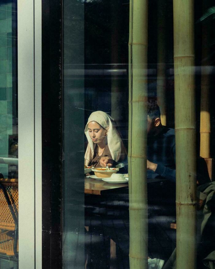 Woman wearing a headscarf eating in a restaurant, with natural light creating a scene resembling a Renaissance masterpiece.