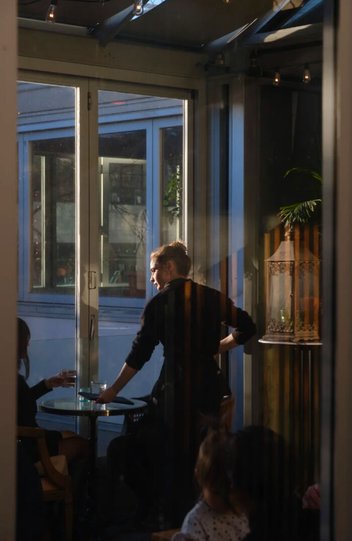 Person serving drinks at a cafe table with natural light, capturing a scene resembling a Renaissance masterpiece.