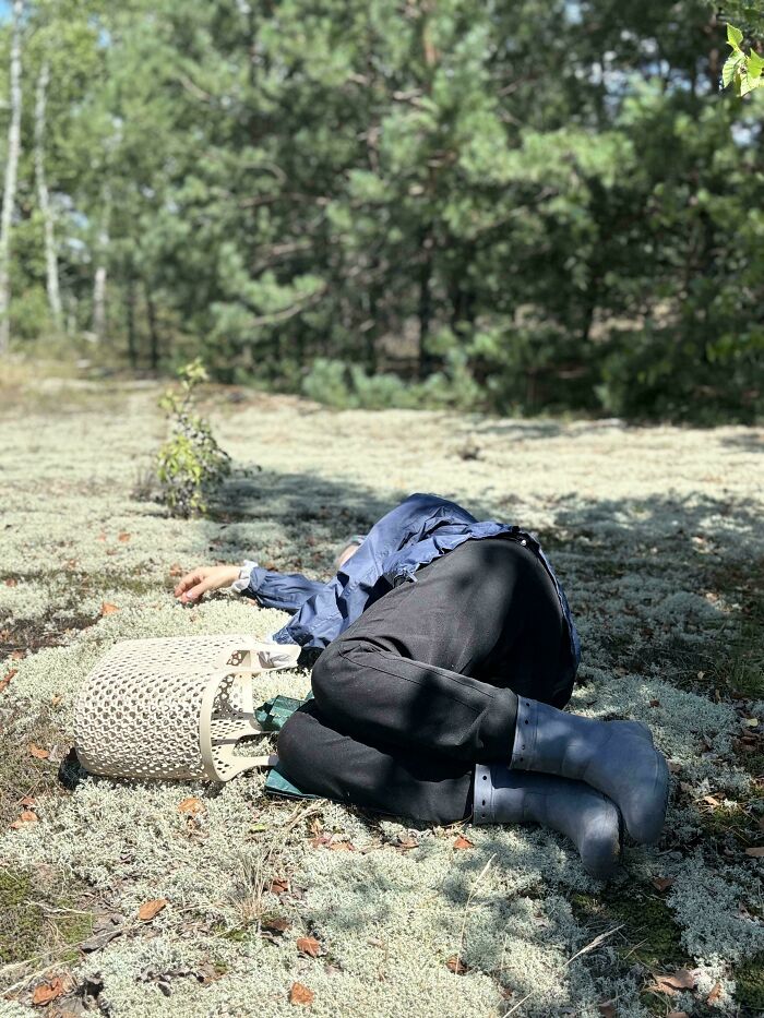 Person in blue jacket and boots lying curled on mossy ground in forest, an accidental renaissance photo style.