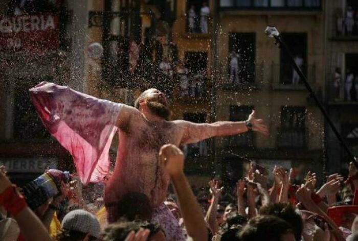 Man drenched in water raising arms joyfully at crowded outdoor festival, capturing accidental Renaissance photo moment.
