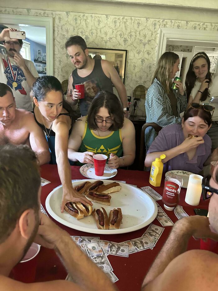 Group of people around a table with hot dogs and drinks, capturing a moment perfect for accidental Renaissance photos.