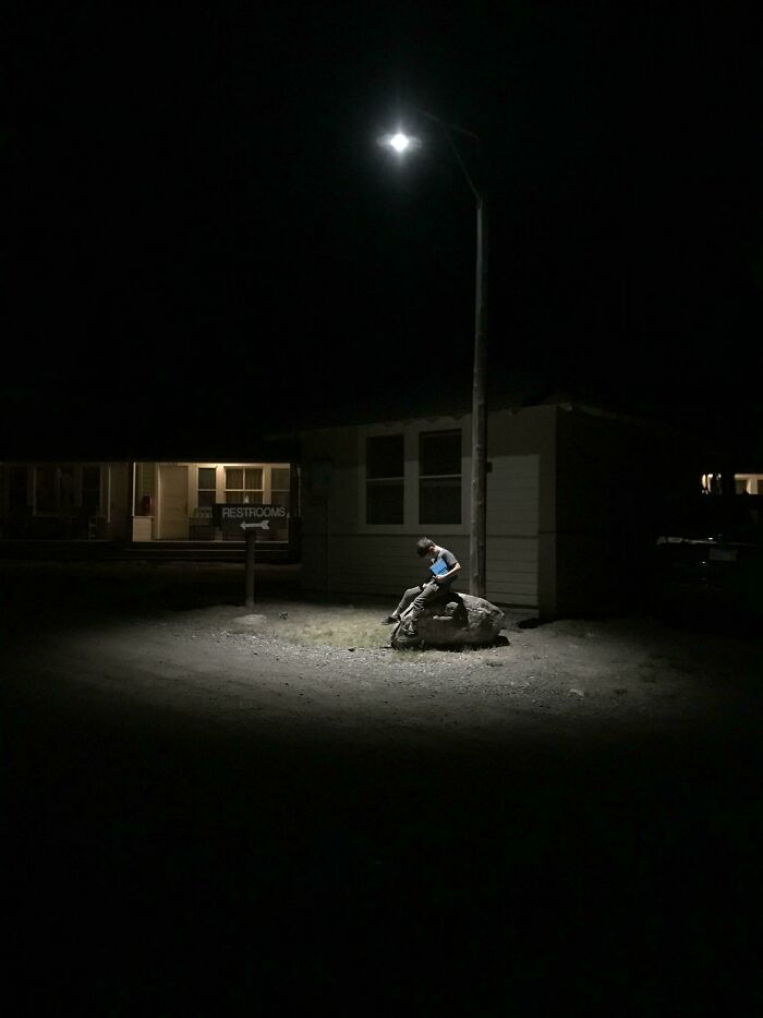Boy sitting on a rock under a streetlamp at night, an accidental Renaissance photo with museum-quality lighting.