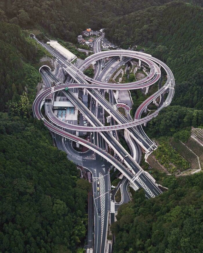 Aerial view of brilliant infrastructure with complex highway interchanges surrounded by dense green forest.