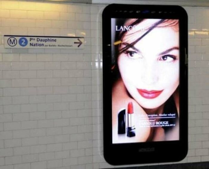 Pantalla digital con publicidad de lápiz labial en estación de metro, ejemplo del aumento del consumismo en publicidad moderna.