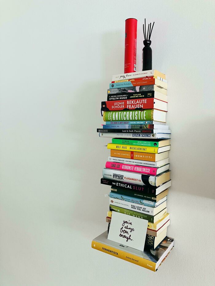 Stack of colorful books with decorative items on top, illustrating the impact of consumerism through book collection.