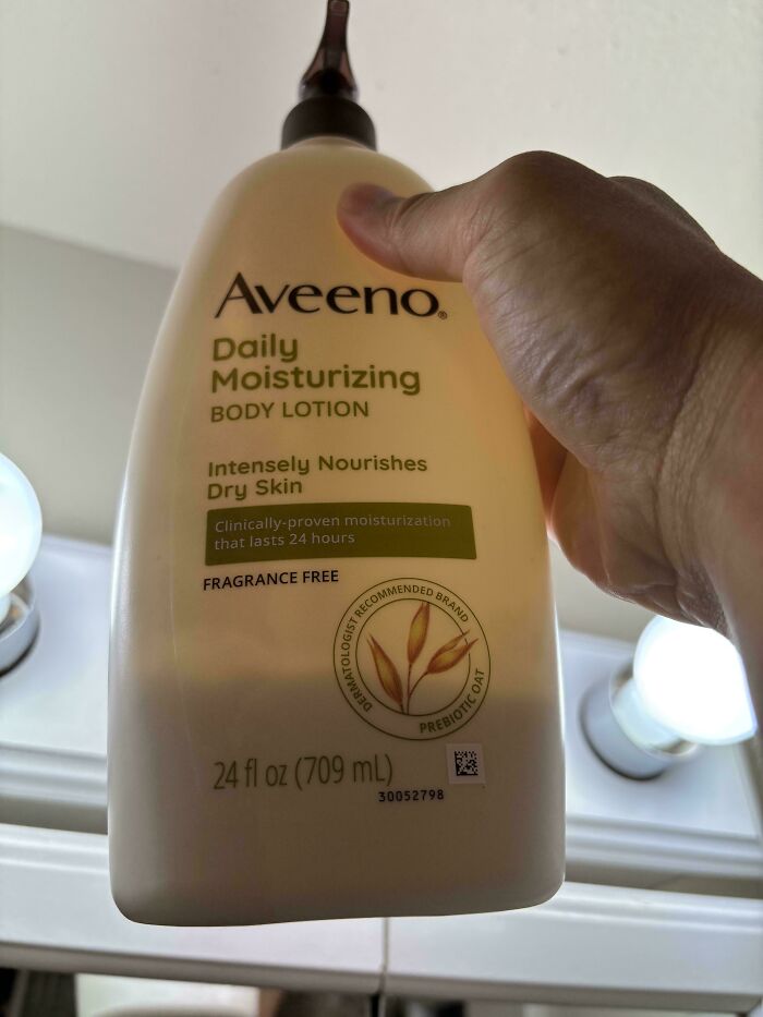 Envase de loción corporal Aveeno Daily Moisturizing en mano, simbolizando consumo y productos de cuidado personal.