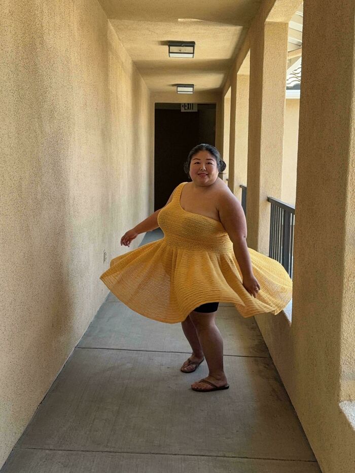 Person wearing a vibrant yellow crochet dress twirling in a hallway, showcasing intricate crochet craftsmanship.
