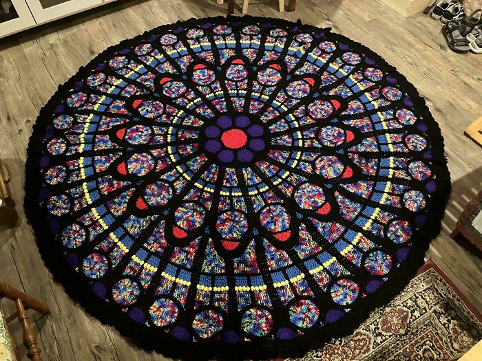 Intricate round crochet blanket with colorful geometric patterns on a wooden floor, showcasing crochet enthusiasts' craftsmanship.