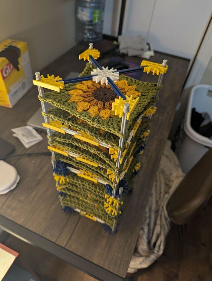 Stacked sunflower crochet squares held together by plastic rods and connectors, showcasing intricate crochet craftsmanship.