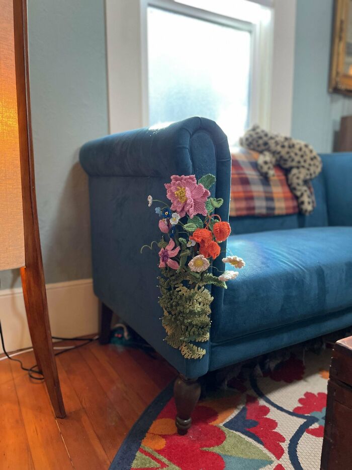 Blue couch with intricate crochet flowers and greenery cascading down the armrest in a cozy living room.