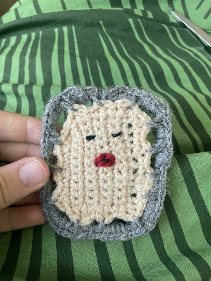 Crochet enthusiast holding a small beige and gray crocheted piece with embroidered face details.
