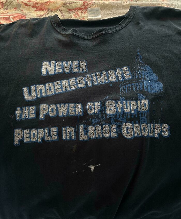 Black t-shirt with faded text warning about the power of stupid people in large groups, reflecting aged like wine predictions.