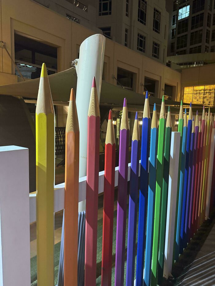 Fence made of oversized colored pencils, showcasing smart and cool design creativity in a public space at night.