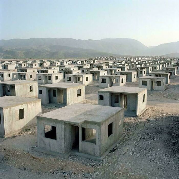 Rows of unfinished concrete buildings in a deserted $58 billion ghost city with barren land and mountains in the background.