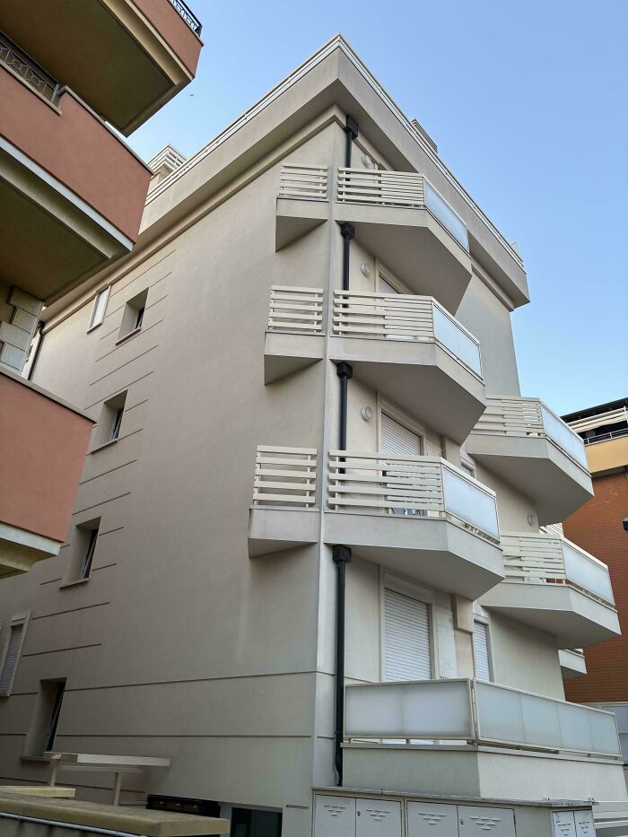 Modern urban building with multiple balconies and closed windows under a clear blue sky in an urban hell setting.