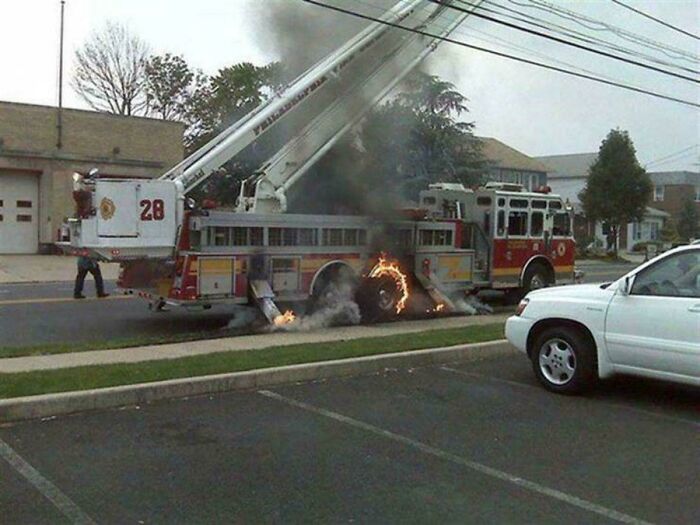 A fire truck with an extended ladder, its rear wheel on fire, emitting smoke. A true accident, this looked expensive.