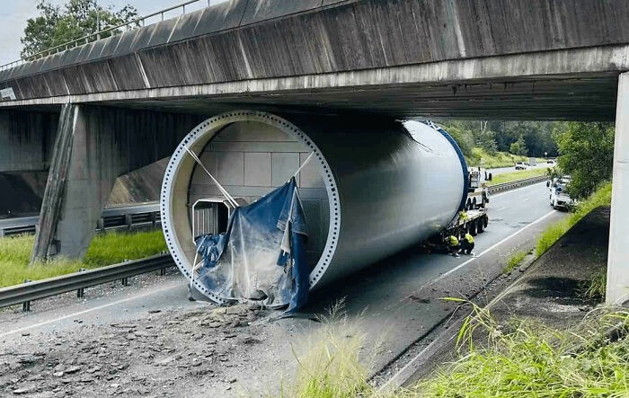 A large wind turbine section stuck under a highway bridge, causing an accident and damage. Looks expensive!