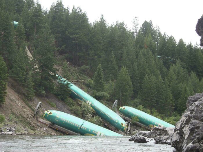 Plane fuselages, victims of a train derailment, lie scattered on a steep, forested riverbank; a true accident and fail.