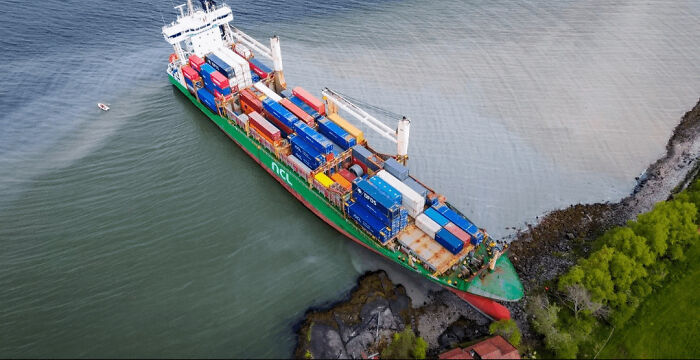 An aerial view of a massive container ship beached on a rocky shore, highlighting one of many accidents and fails.