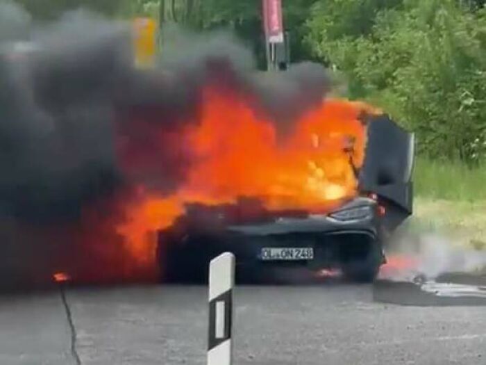 A black car engulfed in bright orange flames and thick black smoke on a road, a costly accident that looked expensive.