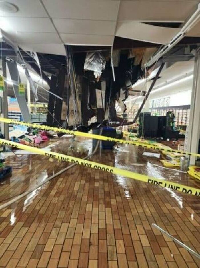 A supermarket with a collapsed ceiling, water on the floor, and yellow "FIRE LINE DO NOT CROSS" tape. An expensive accident.