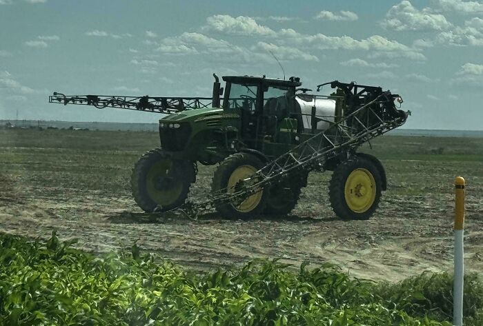 A green John Deere crop sprayer tractor with wide boom arms in a field. A potential farming accident.