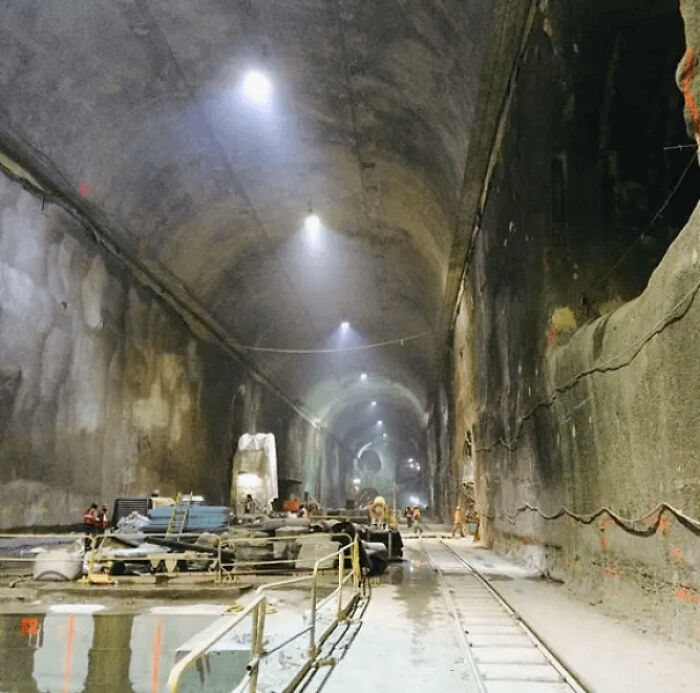 An extremely large and eerie construction tunnel with workers, equipment, and rail tracks, highlighting the scary scale.