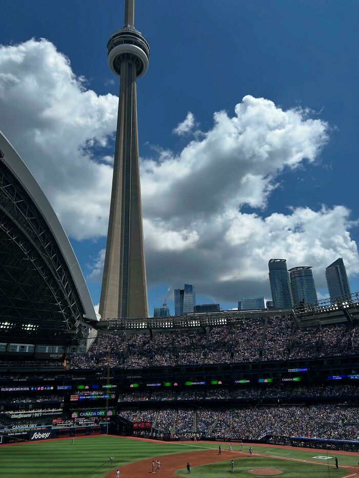 The CN Tower overlooking a filled baseball stadium, an extremely large structure creating a scary and eerie urban landscape.