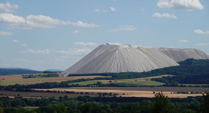 An extremely large salt mountain towering over a vast landscape of fields and forests, showcasing eerie scale.