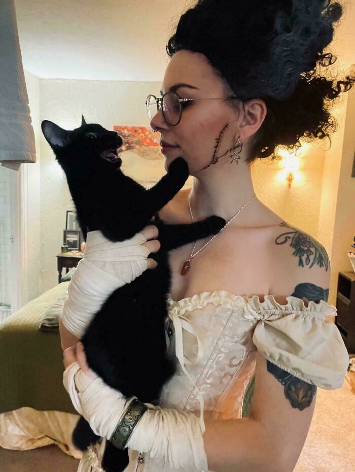 Woman in costume holding a black cat with mouth open, showing cats who couldn’t keep their meows to themselves.