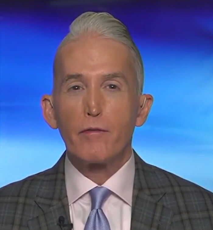 Man with an unfortunate haircut, a high silver pompadour, wearing a suit and tie.