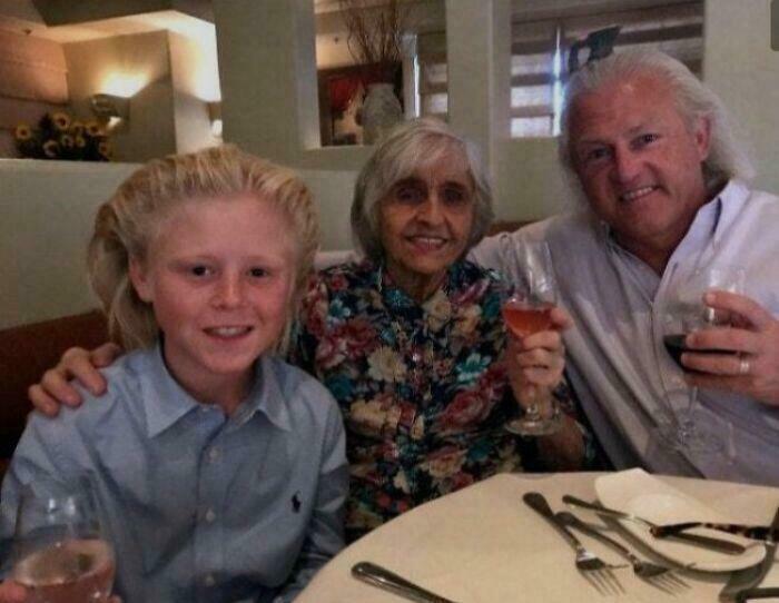 A young boy with an unfortunate haircut, an older woman, and a man smiling together at a dining table.