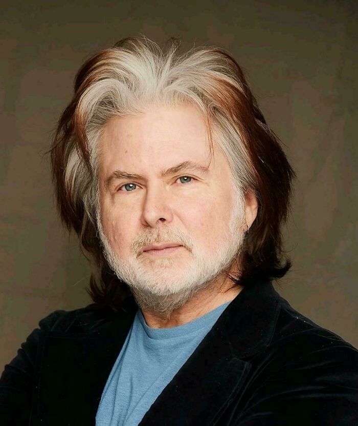 A man with a serious expression, displaying one of many unfortunate haircuts, with a mix of brown and grey hair.