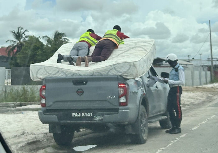 Two employees blatantly ignoring safety protocol by lying on a mattress unsecured on a moving pickup truck.