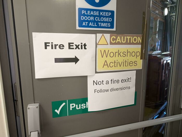 Door covered with conflicting safety signs showing poor safety protocol and dangerous workplace decisions.