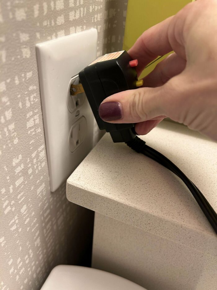 Hand plugging a power adapter into an outlet blocked by a countertop edge in a perfect preventable fail photo.