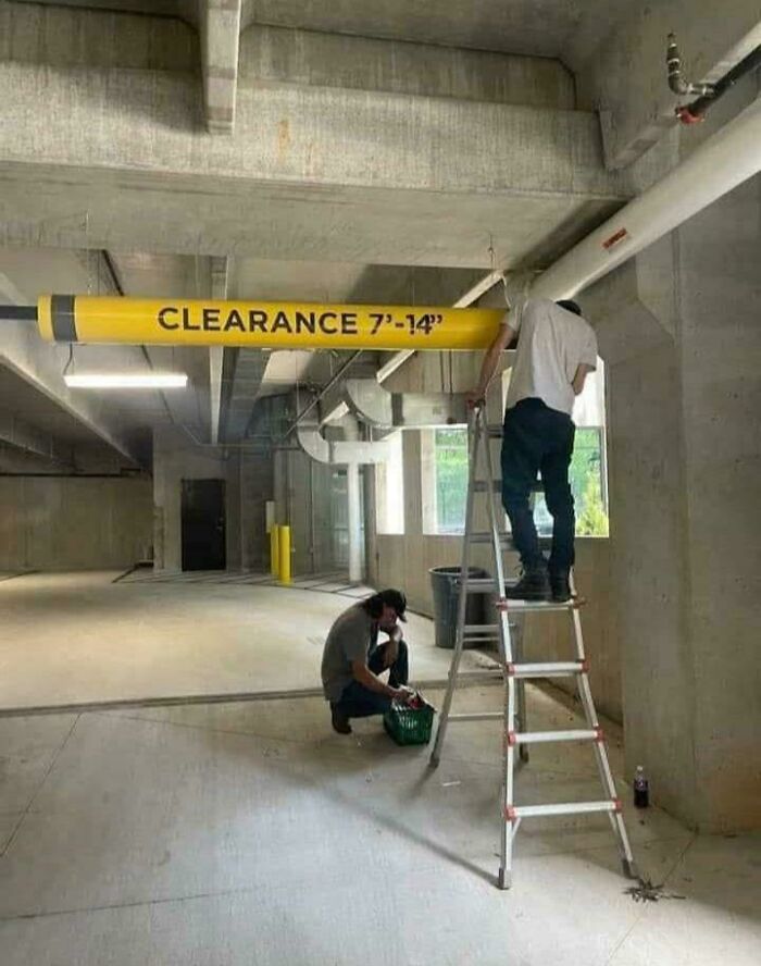 Two workers in a garage near a clearance bar that is too low, illustrating a hilarious preventable fail moment.