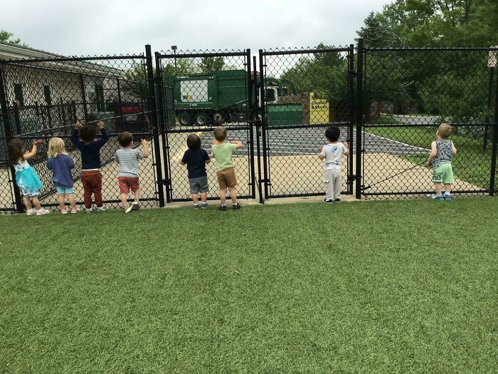 Group of toddlers standing by a chain-link fence on grass, capturing wholesome dads parenting moments outdoors.
