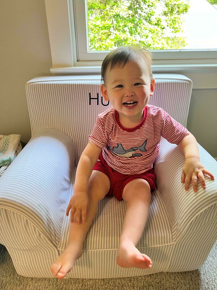 Smiling toddler sitting on a striped chair in a bright room, capturing wholesome dads parenting moments.