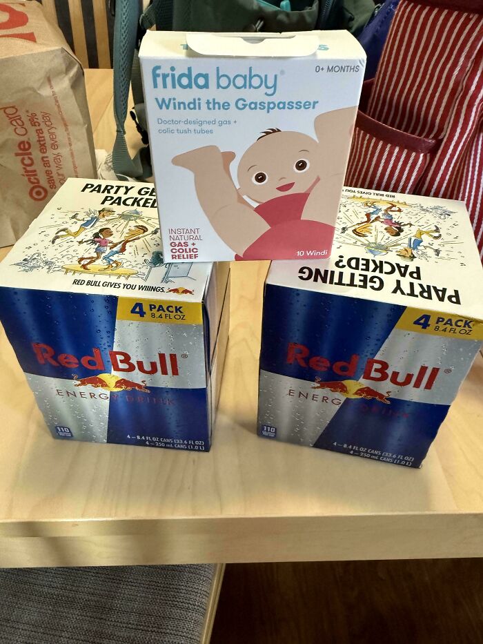 Two packs of Red Bull energy drink and a box of Frida Baby gas and colic relief on a table, showing parenting essentials.
