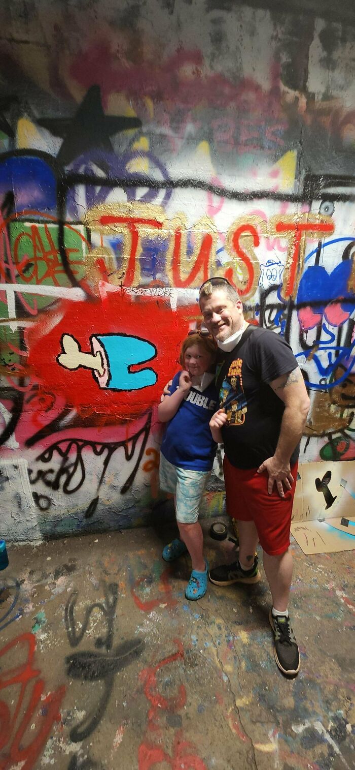 A dad and child smiling together in front of vibrant graffiti wall, capturing wholesome parenting moments.