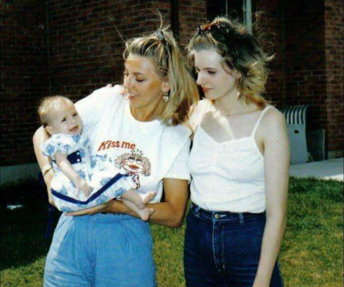 Two women outdoors holding a baby, capturing a candid glimpse into the past with vintage casual clothing and hairstyles.