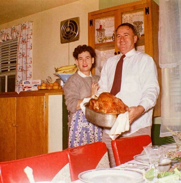 Couple in a vintage kitchen presenting a cooked turkey, a candid glimpse into the past not found in history books.