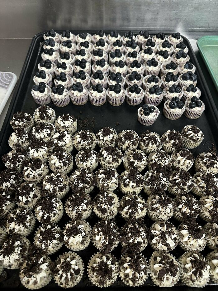 Tray of incredible bakes featuring mini blueberry and cookies-and-cream cupcakes arranged on a dark baking sheet.