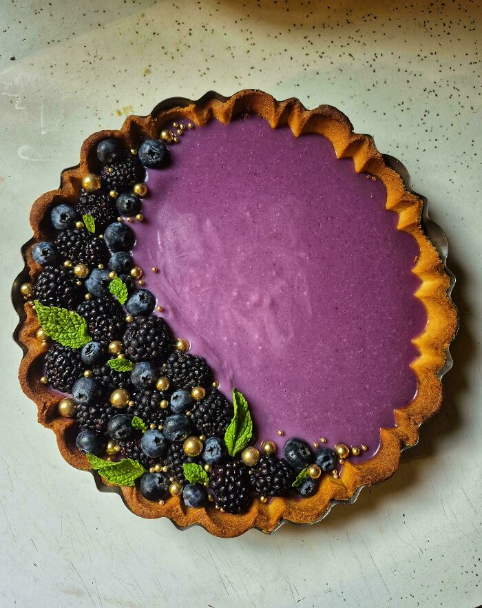 Purple berry tart with fresh blackberries, blueberries, mint leaves, and golden edible pearls, a stunning example of incredible bakes.